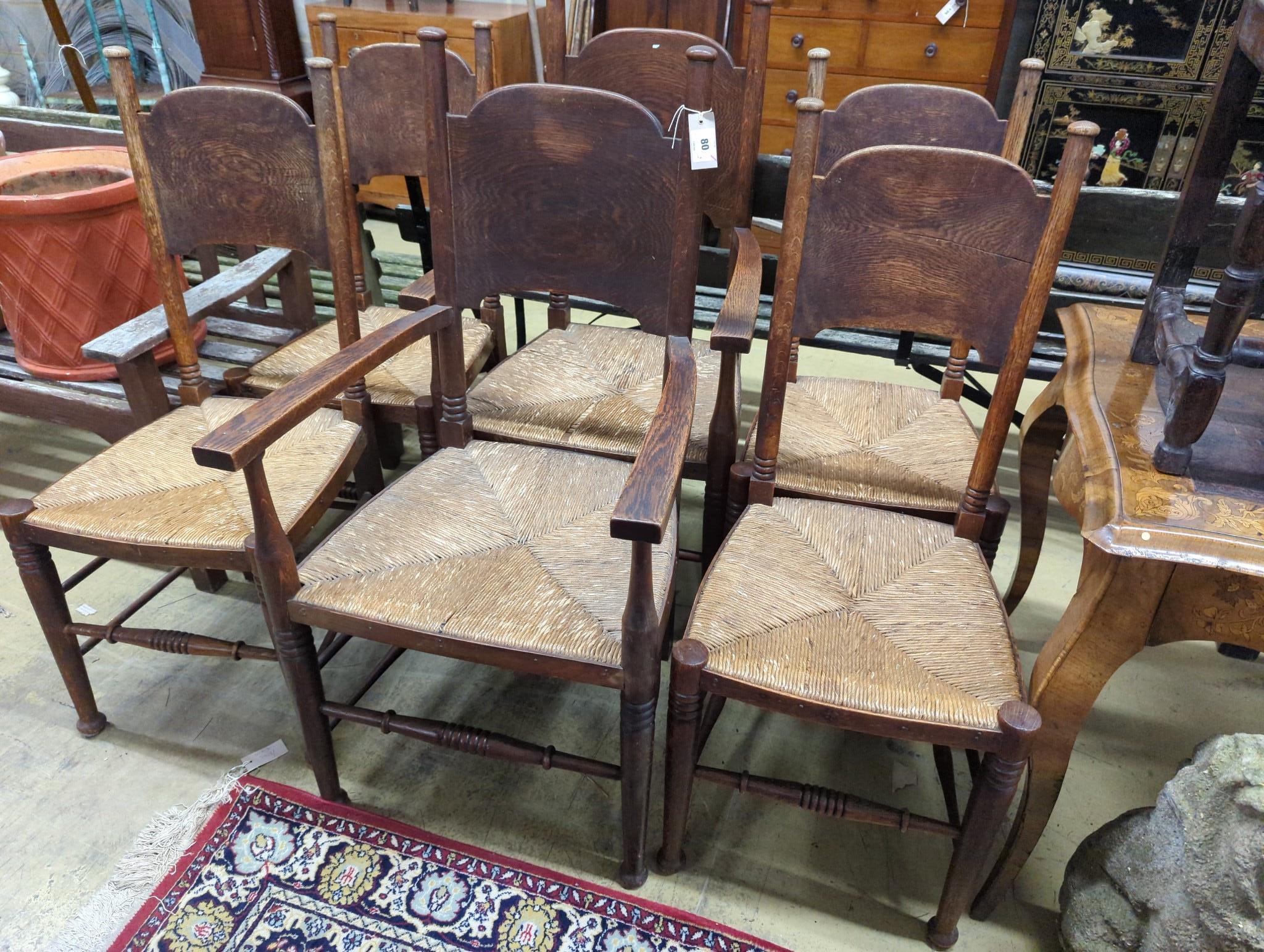 A set of six Arts & Crafts oak chairs, including a pair of carvers, in the Glasgow School manner by William Birch, High Wycombe, with shaped panels backs, ring turned frames and rush seats, carvers W.58cm D.54cm H.109cm